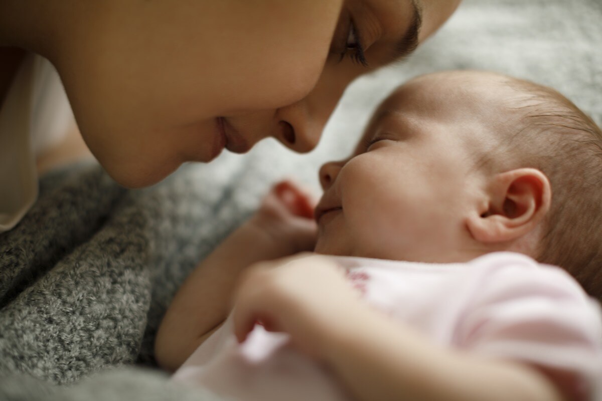 Uma mãe observa de perto seu bebê dormindo, representando os benefícios de trabalhar em uma empresa participante do Programa Empresa Cidadã, que permite mais tempo dedicado à família.